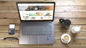 silver laptop next to coffe cup smartphone and glasses