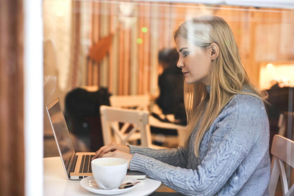 serious young woman using netbook while having hot drink in modern cafe