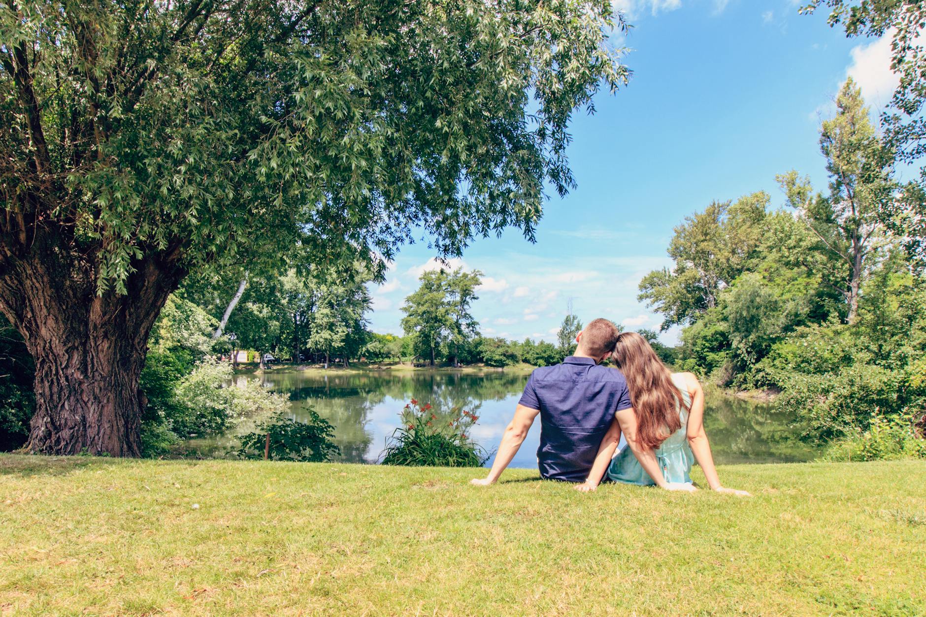 couple sitting on grass field in front of body of water