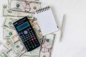 calculator and notepad placed over stack of paper bills