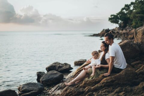 man and woman sitting on rock near seashore