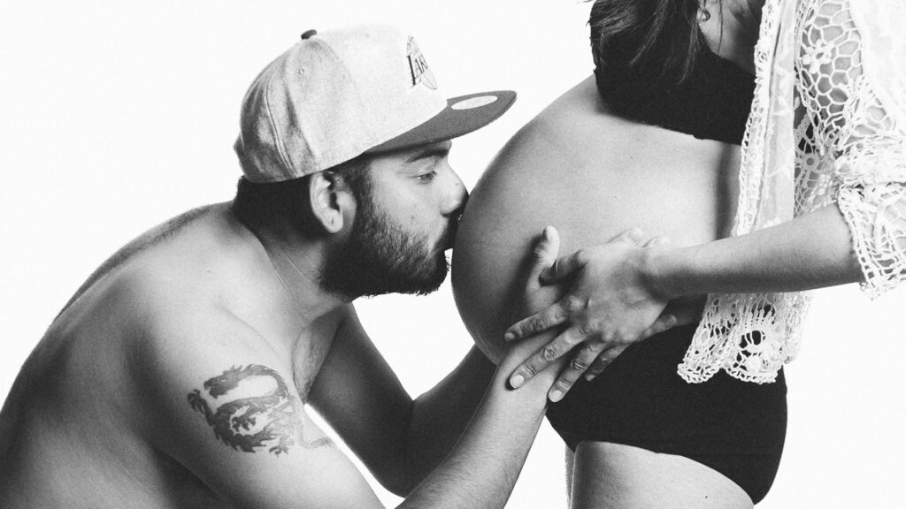 grayscale photography of man kissing woman s pregnant bell