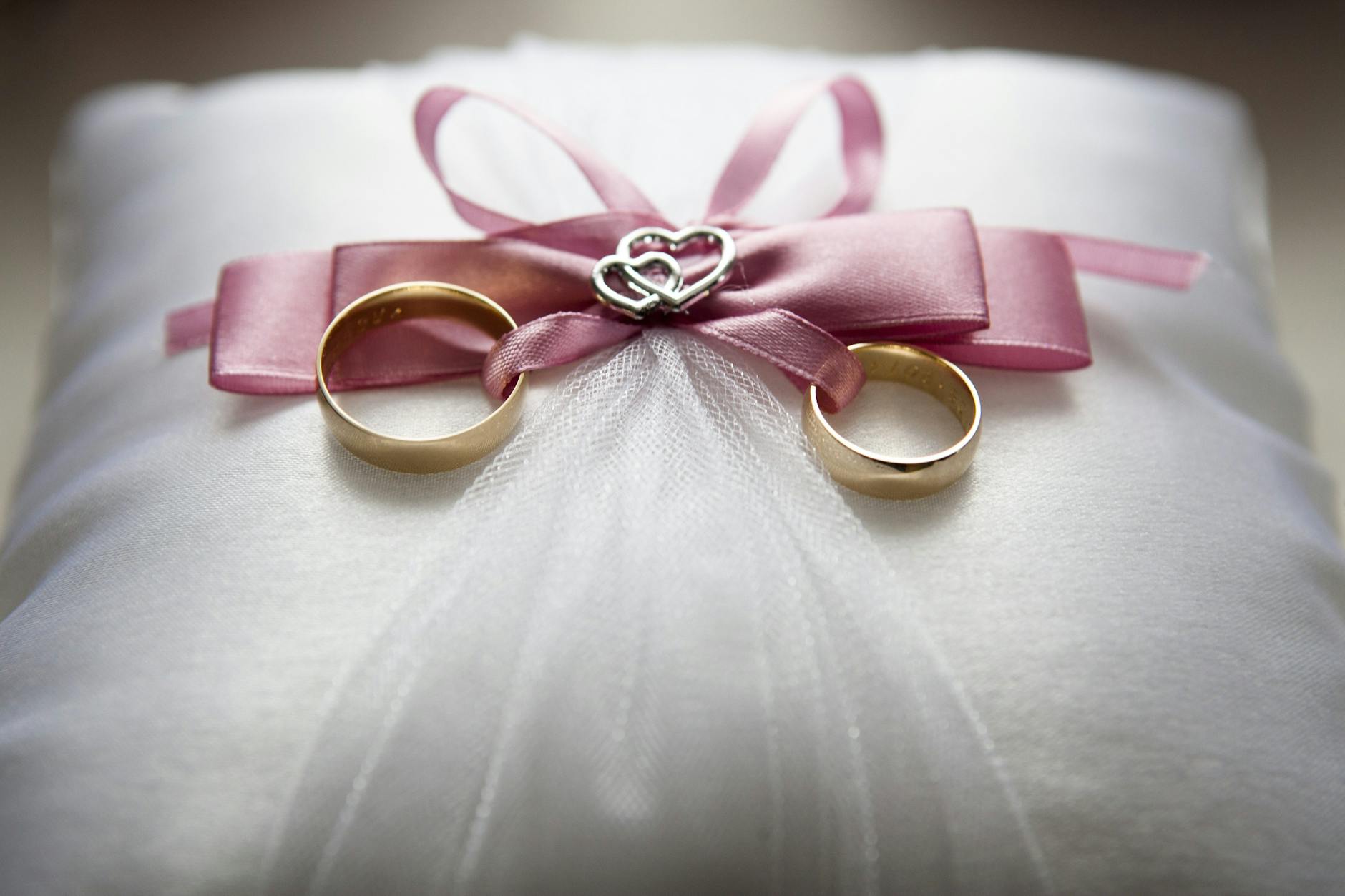 selective focus photography of silver colored engagement ring set with pink bow accent on throw pillow