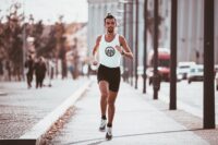 active young man running along asphalt sidewalk