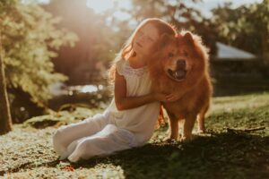 girl hugging adult chow chow sitting on grass field