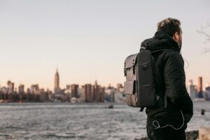 man wearing black bubble jacket and black leather backpack near bay